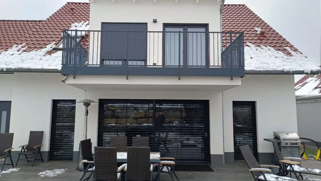 Terrassenseite eines Wohnhauses mit bodentiefer Schiebetür, außenliegende Raffstore heruntergelassen