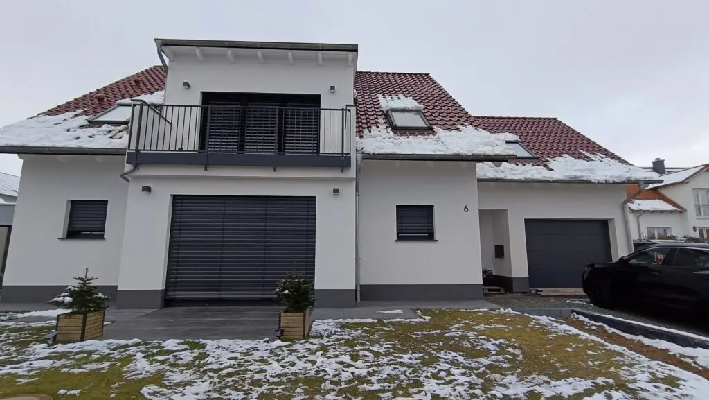 Wohnhaus mit anthrazitfarbenem Garagentor, darüber Balkon mit Raffstore