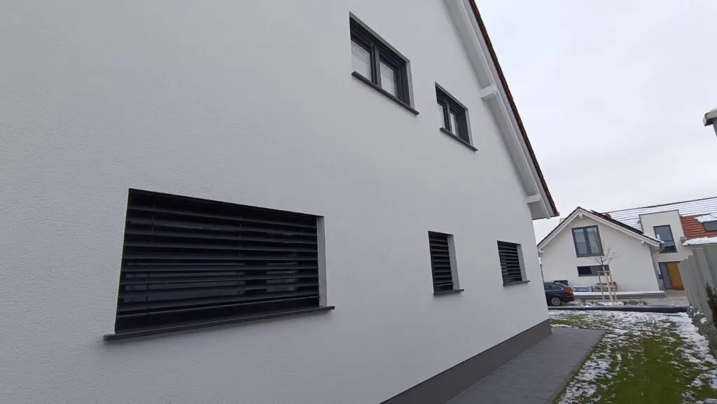 Giebelseite mit dunkel gerahmten Fenstern und geschlossenem Raffstore am großen Fensterelement
