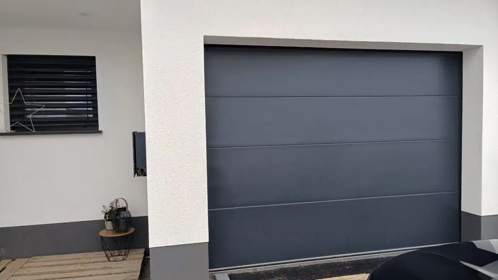 Anthrazitfarbenes Sektionaltor neben einem Fenster mit Raffstore