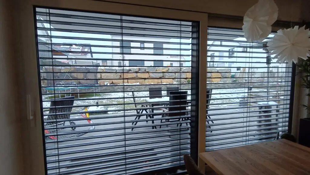 Blick von innen durch geschlossene Raffstore-Lamellen auf die Terrasse