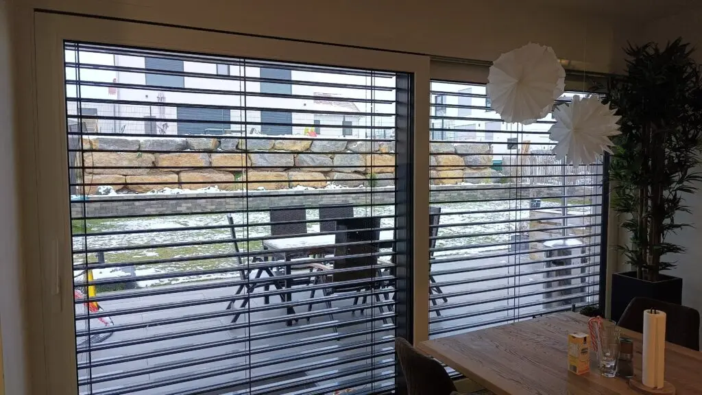 Blick von innen durch Raffstore mit gedrehten Lamellen: Tageslicht kommt herein, Sonne bleibt draußen